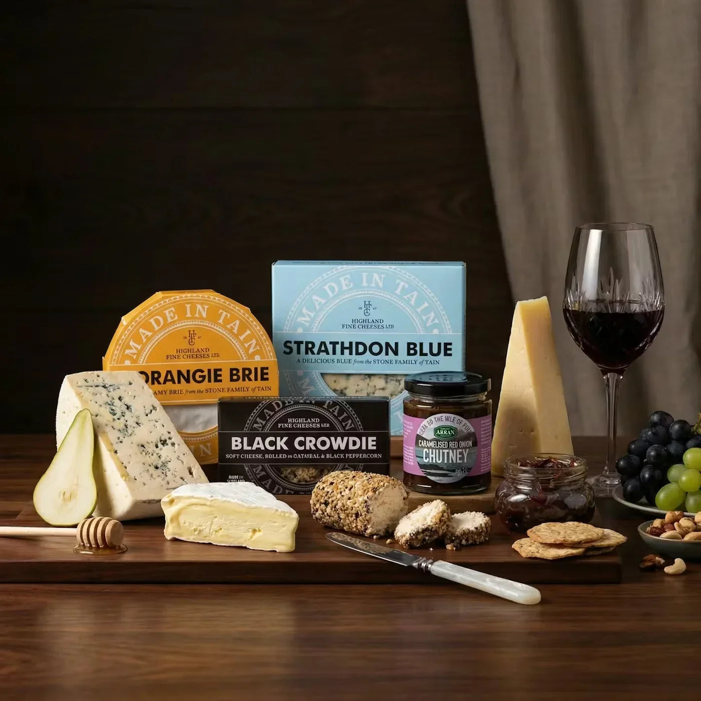 Scottish cheeses with labelled packs, oatcakes, chutney and red wine on a wooden board