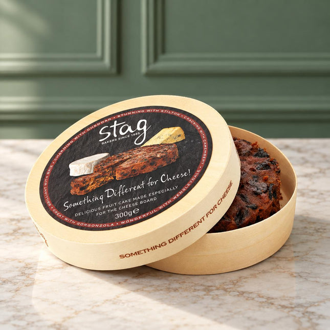 A round beige paperboard box for Stag Making Cheese, shown open with a fruit cake inside. The lid features a circular label with the Stag logo and the text 'Something Different for Cheese!'.