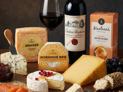 Assorted cheeses, a bottle of red wine, and a glass on a wooden table with a dark background.