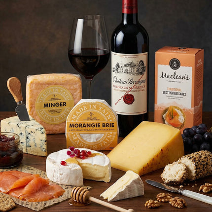 Assorted cheeses, a bottle of red wine, and a glass on a wooden table with a dark background.