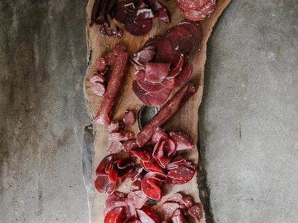 Wooden board with various cured meats on a concrete surface