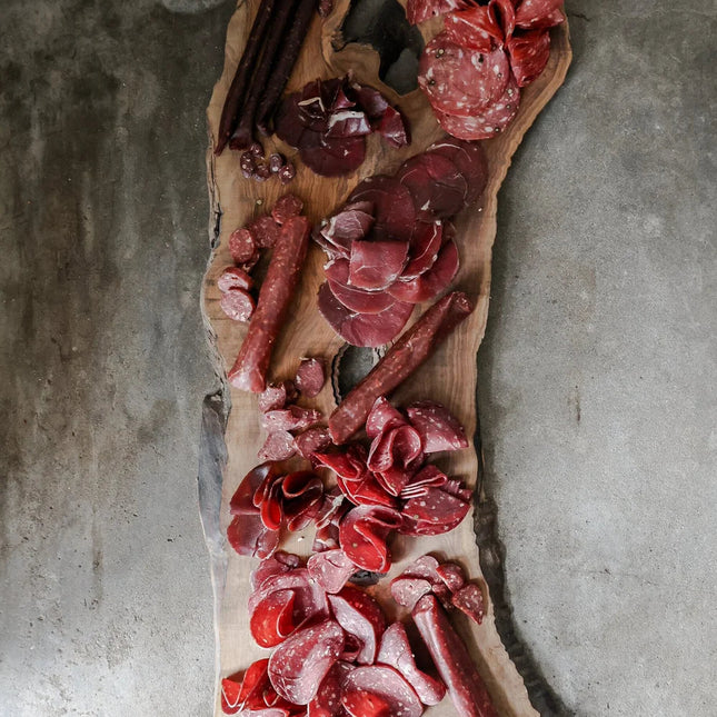 Wooden board with various cured meats on a concrete surface