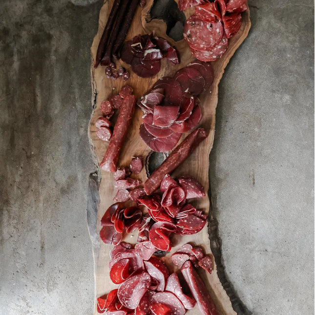 Wooden board with various cured meats on a concrete surface